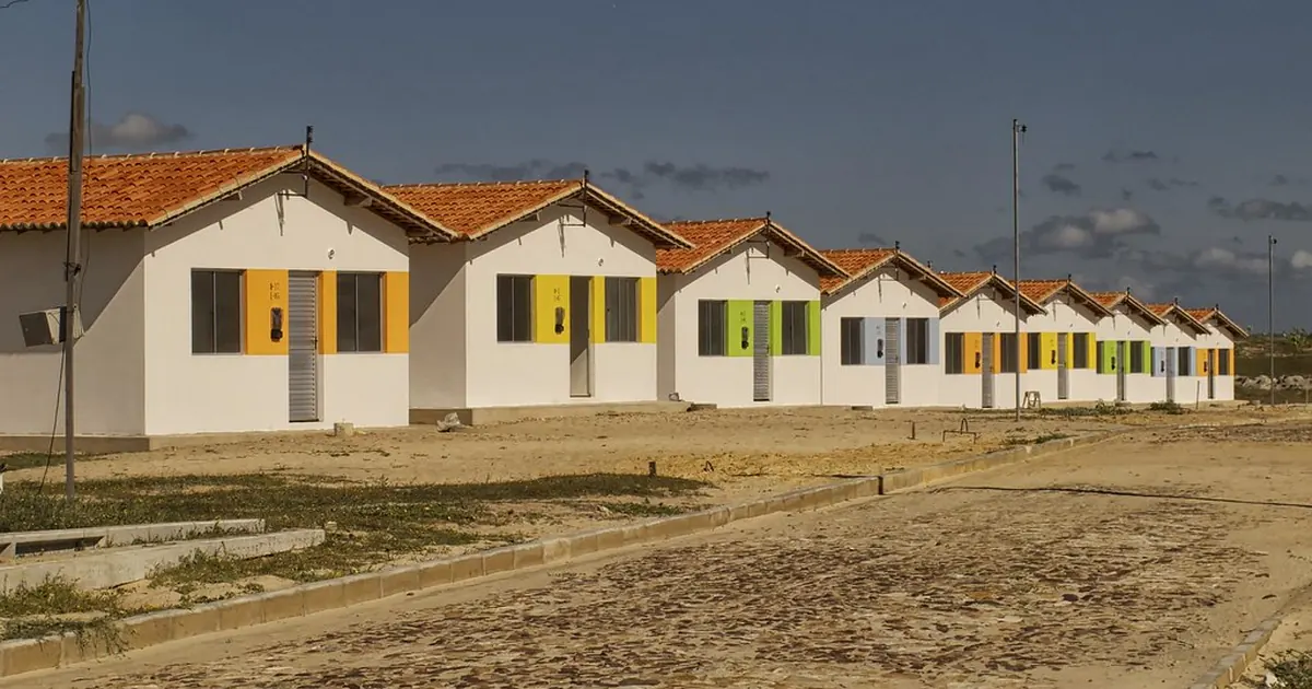 Fileira de casas térreas novas, de telhado de barro e portas coloridas, numa rua recém-calçada
